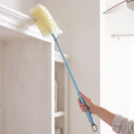 Blue-handled extendable duster being used to clean the top edge of a shelf