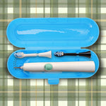 Open blue toothbrush travel case containing an electric toothbrush handle and two replacement brush heads on plaid background.