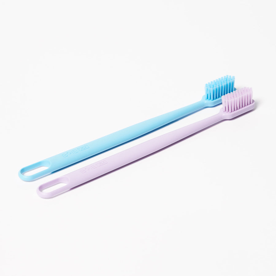Two slim toothbrushes lying flat on white background, one blue and one light purple