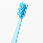 Single blue toothbrush shown diagonally with dense extra-soft bristles against white