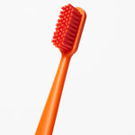 Tight angled close-up of an orange Boie toothbrush showing dense soft bristles and smooth handle on white background.