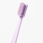 Single light purple toothbrush shown diagonally with dense bristles on white background