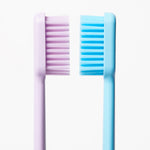 Side-by-side profile view of two toothbrush heads, blue and light purple, showing bristle depth