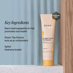 Boka Kids Orange Cream toothpaste tube on a textured ledge with text listing key ingredients and a fluoride-free badge.