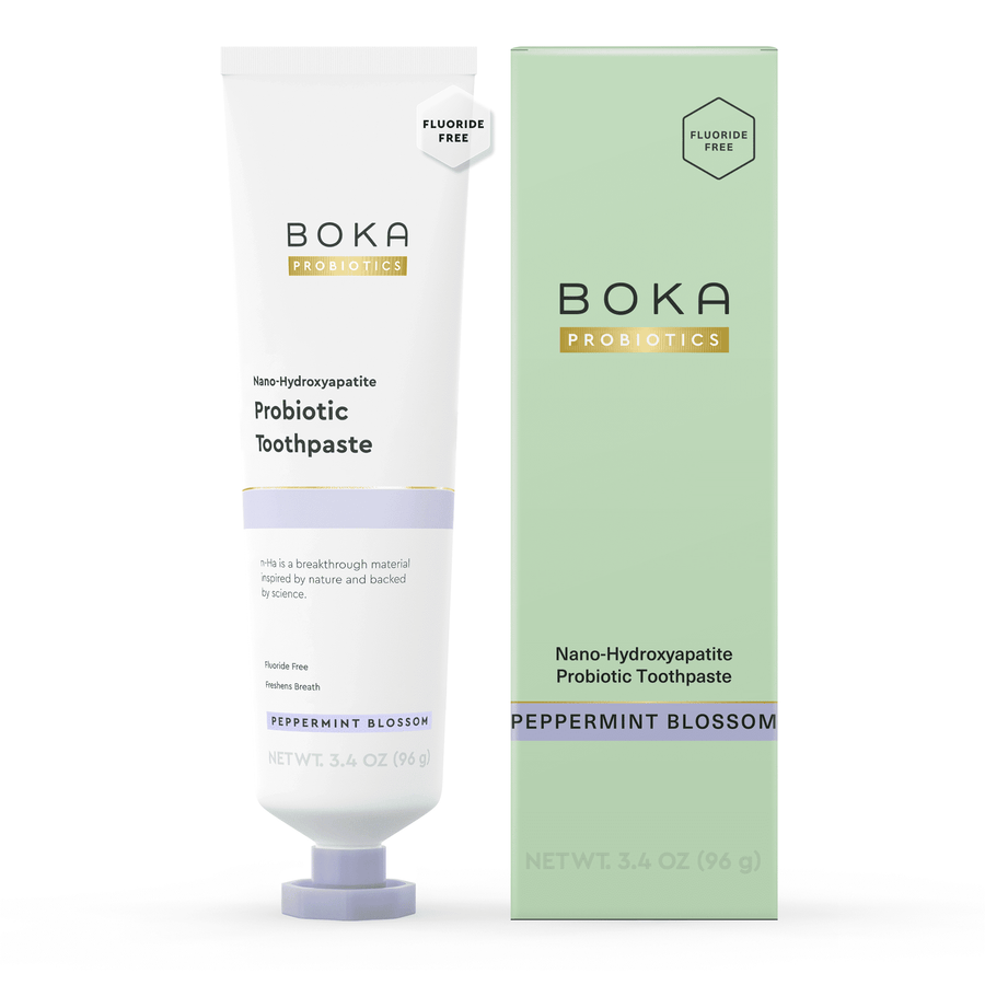 White Boka Probiotics toothpaste tube standing next to its pale green boxed packaging on a white background.