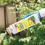 Gloved hand tipping a Bonide Go Away! repellent bottle to pour granules near green plants and foliage