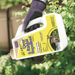 Hand holding a tilted Bonide Go Away! Deer & Rabbit Repellent jug over garden foliage, granules visible