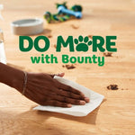 Hand wiping a wooden surface with a paper towel amid pet-related debris and headline “Do More with Bounty”