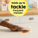Hand wiping a spill with a Bounty Essentials paper towel with circular callout reading 'holds up to tackle frequent messes'.
