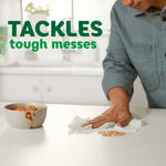 Person using a paper towel to clean tomato sauce splatter from a white countertop with text about tackling tough messes