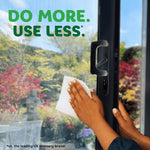 Hands cleaning a glass door or window with a Bounty paper towel against a blurred outdoor garden backdrop and product slogan.