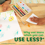 Hand wiping watercolor paint spills on a wooden table with a paper towel, art set and paper visible nearby