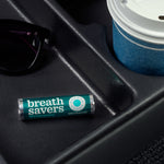Lifestyle shot of a Breath Savers Wintergreen roll resting in a vehicle cup-holder area next to sunglasses and a paper cup.