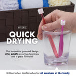 Hand placing two small Brilliant toothbrushes into a clear cup to demonstrate quick-drying design beside towel-lined basket.