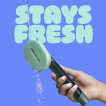 Water pouring over a green foam scrubber attached to a dishwand held in a hand with 'STAYS FRESH' text above