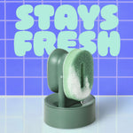 Brite palm scrubber on its drain-and-dry stand with foam and water drip, blue tiled background and “STAYS FRESH” text