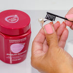 Person holding a pearl ring while brushing it with a small black brush next to a Connoisseurs cleaner jar