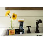 Lifestyle scene of Burt's Bees Charcoal + Whitening toothpaste tube and box placed on a bathroom counter with flowers in a vase