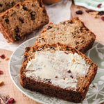 Buttered slices of loaf cake on a patterned plate with additional slices and crumbs on a wooden surface.