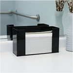 Black countertop dispenser holding a stack of white C-fold hand towels beside a bathroom mirror and vase