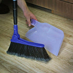 Blue broom and translucent dustpan placed on wood floor with a hand holding the dustpan