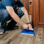 Lifestyle image of someone sweeping with a Camco blue dust pan and whisk broom on flooring