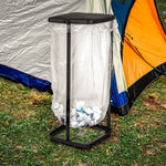 Collapsible trash bag holder with lid and a clear bag, shown outdoors next to a camping tent on grass