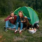 Couple sitting by a green tent outdoors with a gray collapsible basin on the grass filled with ice and bottled drinks.