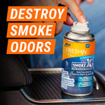 Hand pressing nozzle on a can of Armor All FRESHfx Smoke X placed in a car cupholder with bold ‘Destroy Smoke Odors’ text