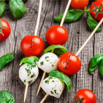 Caprese-style skewers of cherry tomatoes, basil leaves and mozzarella balls arranged on a wooden surface