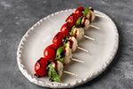 Caprese-style skewers of cherry tomatoes, mozzarella and basil drizzled with balsamic and held by toothpicks