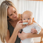 Caregiver holding a baby while gently brushing the infant's mouth with a light green silicone finger toothbrush