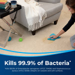 Lifestyle scene of a person dabbing a carpet stain with a blue cloth next to a couch and pet toys, with 'Kills 99.9% of Bacteria' banner