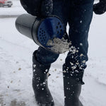 Person using Chapin hand spreader to cast ice melt over snowy pavement in winter