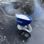 Blue Chapin hand-crank spreader filled with white ice-melt pellets sitting on icy pavement outdoors.