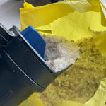 Chapin spreader tipped into a yellow bag while scooping coarse ice melt granules
