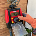Chapin dual-zone water timer mounted on an outdoor spigot with a gloved hand adjusting the control dial