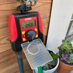 Chapin digital water timer attached to a faucet with clear flip cover open and potted succulents nearby
