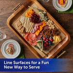 Wooden serving tray lined with unbleached parchment paper displaying a charcuterie-style arrangement of cheeses and fruit