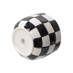 Underside view of a round checkered ceramic planter showing drain hole and glossy black-and-white pattern.