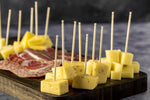 Cheese cubes pierced with decorative wooden toothpicks arranged on a wooden board with charcuterie