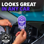 Hand holding a purple Chemical Guys Galactic Scent air freshener hanging inside a car with bold text saying it looks great in any car.