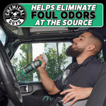 Man spraying Chemical Guys New Car Smell inside a vehicle with a header text panel claiming odor elimination