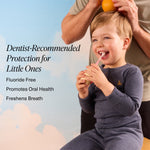 Smiling child holding a toothbrush while an adult places an orange above their head; product benefit text for children's oral care visible.