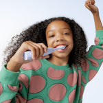 Smiling child using a pale blue battery toothbrush in a lifestyle shot, brushing teeth with one arm raised in the air.