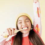 Child smiling and brushing teeth with a yellow Ordo kids sonic toothbrush while wearing a yellow beanie