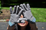 Child holding up G & F suede work gloves toward camera, showing grey palms and striped cuffs