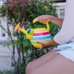 Close-up of a child seated holding a yellow striped bug watering can by the handle and body