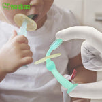 Close-up of a child holding a Haakaa translucent baby toothbrush while a gloved hand demonstrates bristles