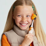Smiling child holding an Ordo Sonic Kids toothbrush with an orange pumpkin Squishmallow character cap against a neutral background